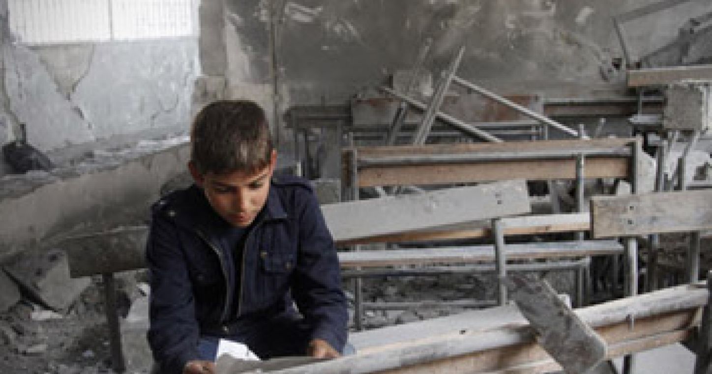 Un niño sirio lee un papel desgarrado dentro de su aula destrozada.